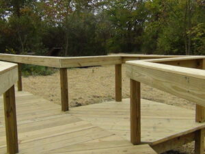 Wooden plank board walk, with hand rails. This board walk is atop the area that will be the wetland that is covered in straw.