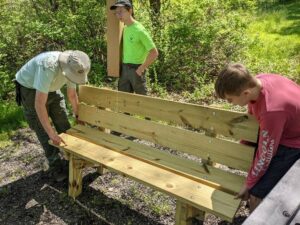 Three boy scout troop members placing the benches they have made on the meditation trail.